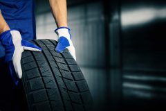 car tire shop and service - mechanic holding new tyre on garage background. copy space